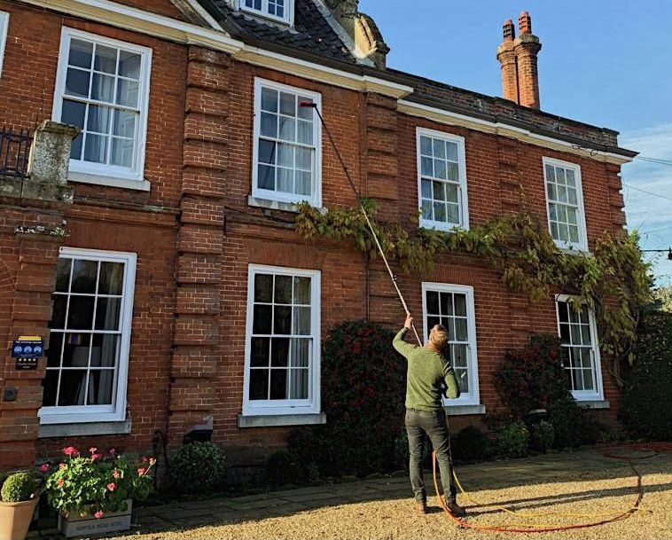 Window cleaner using a water-fed pole on a red-brick house in Norfolk