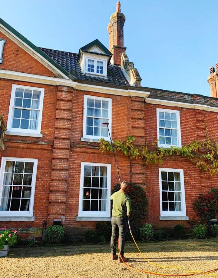 Window cleaner using a water-fed pole on a large red brick house in Suffolk